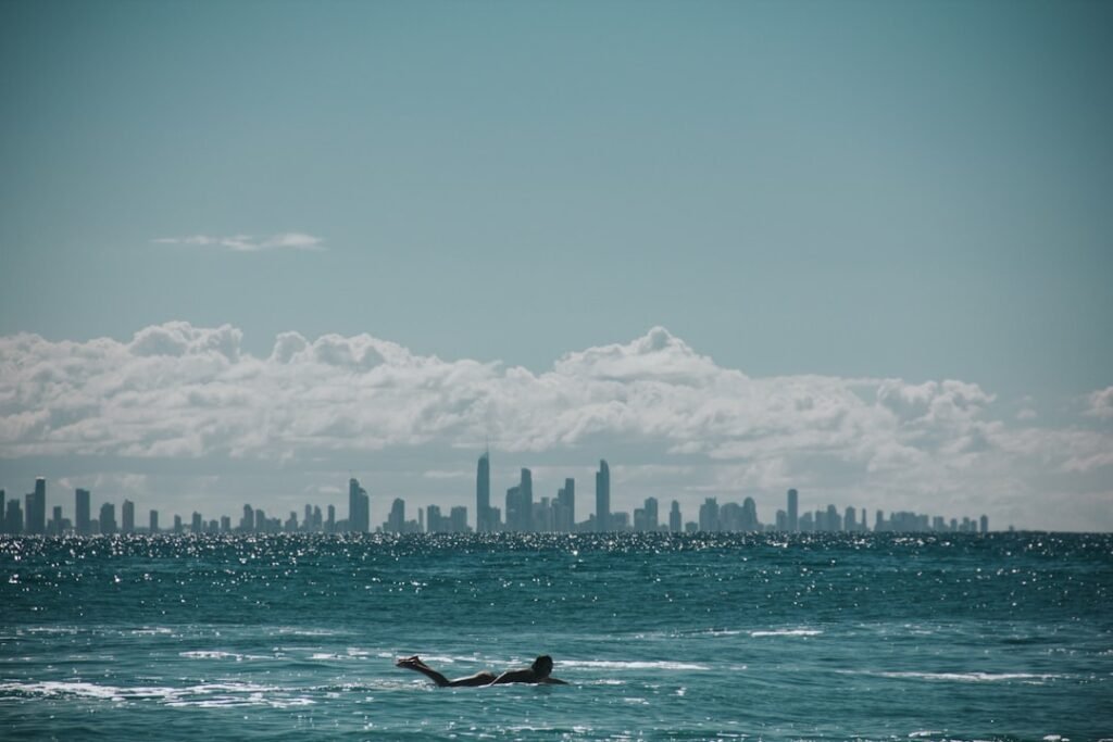 Surfer in the ocean with city skyline in the background.